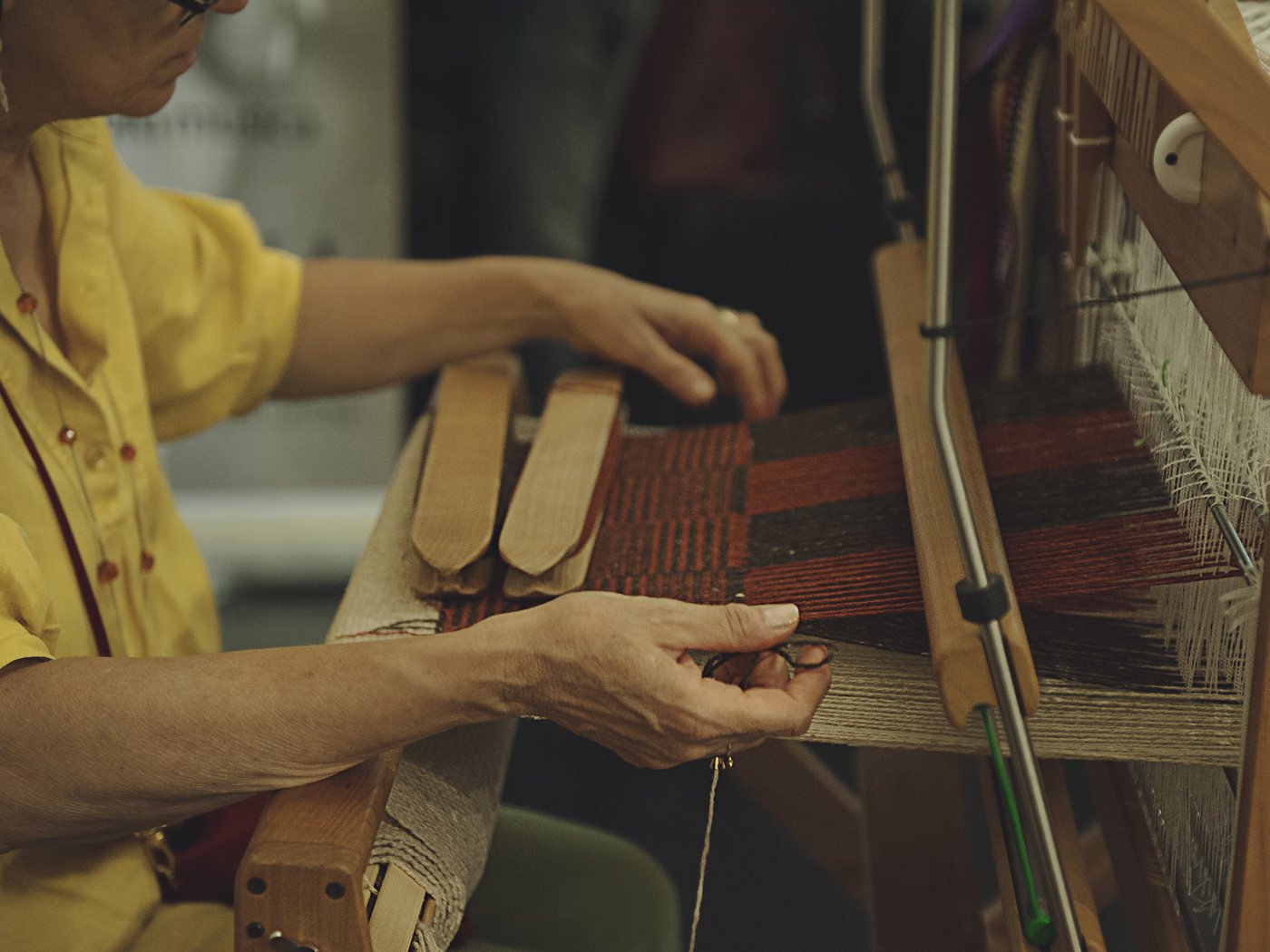 Le mani di una tessitrice al telaio, tra i licci e la trama